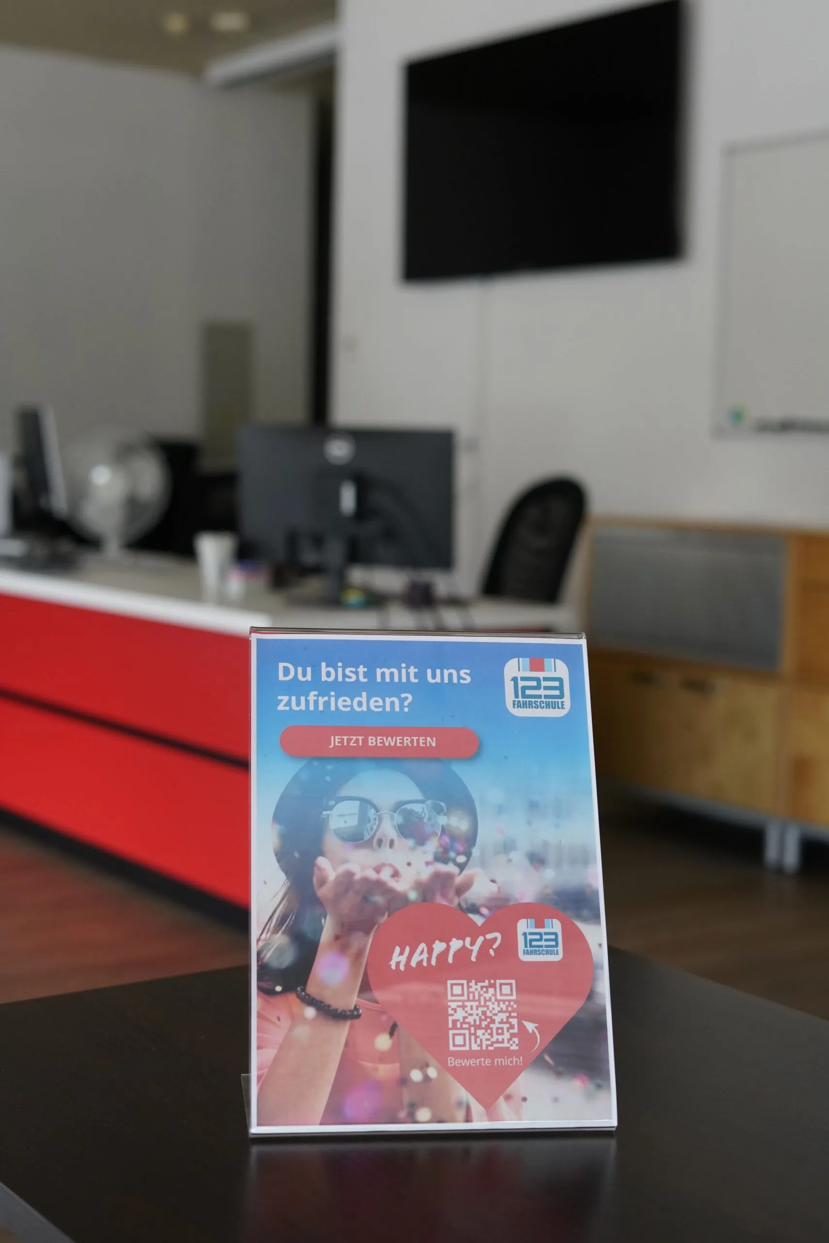 Werbeschild mit der Beschriftung "Bewerte uns" einer Fahrschule steht auf dem Tisch